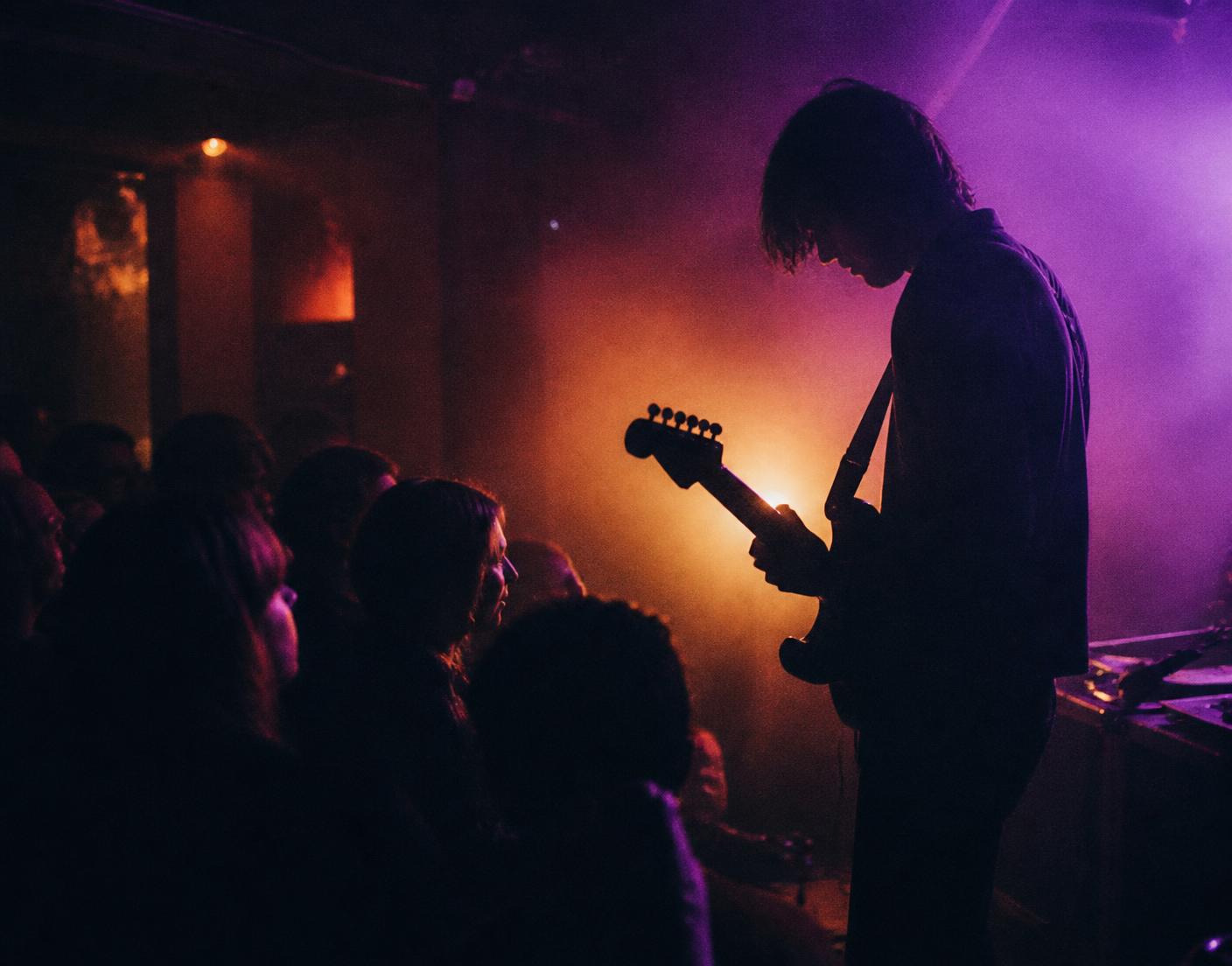 Silhouette of a guitarist on a small stage in front of a close crowd