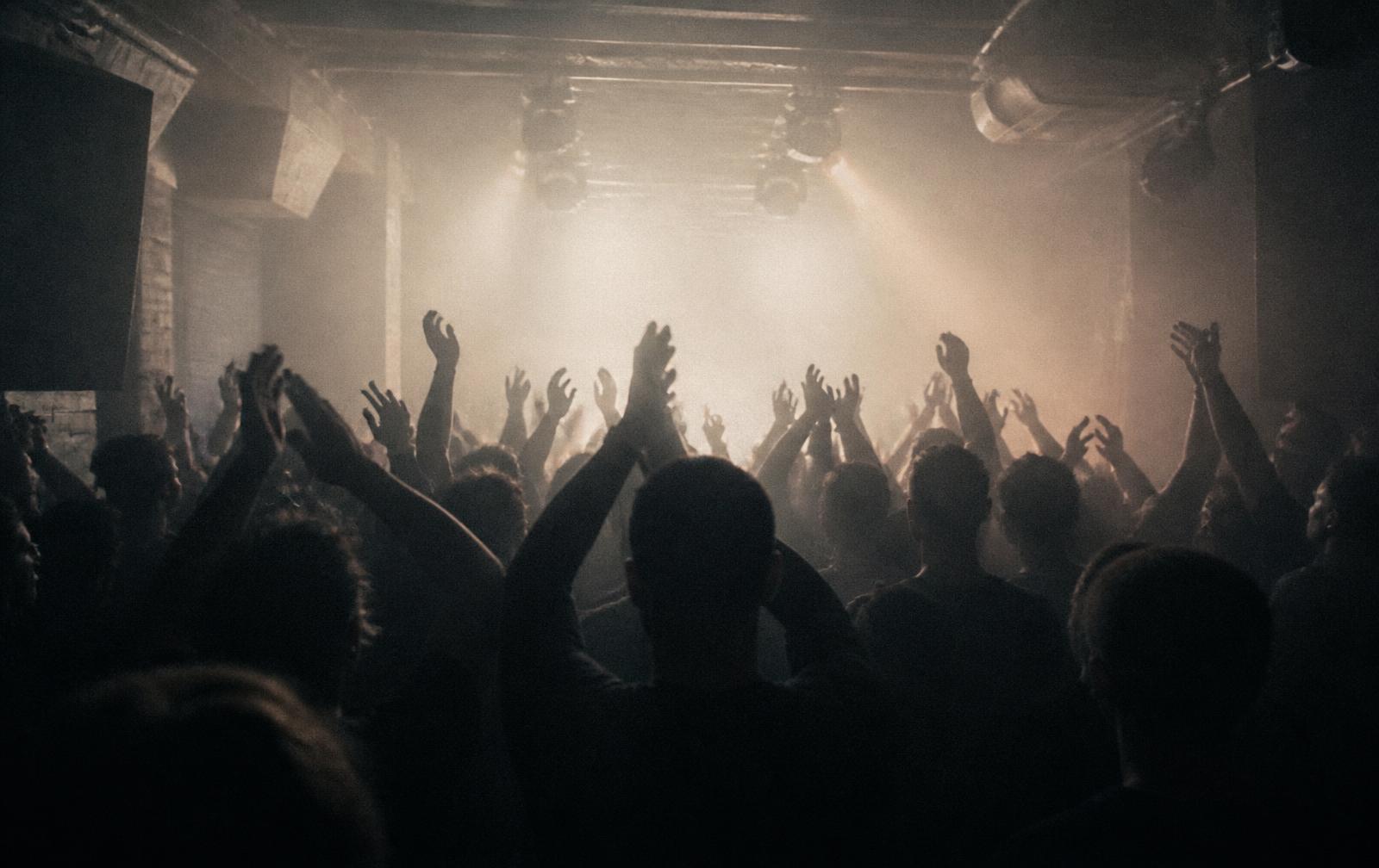 Crowd silhouettes with raised hands as house lights come up